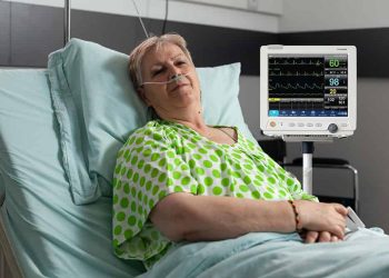 Portrait of sick pensioner woman looking into camera while resting in bed recovering after medical surgery in hospital ward. Hospitalized patient waiting for healthcare treatment during examination